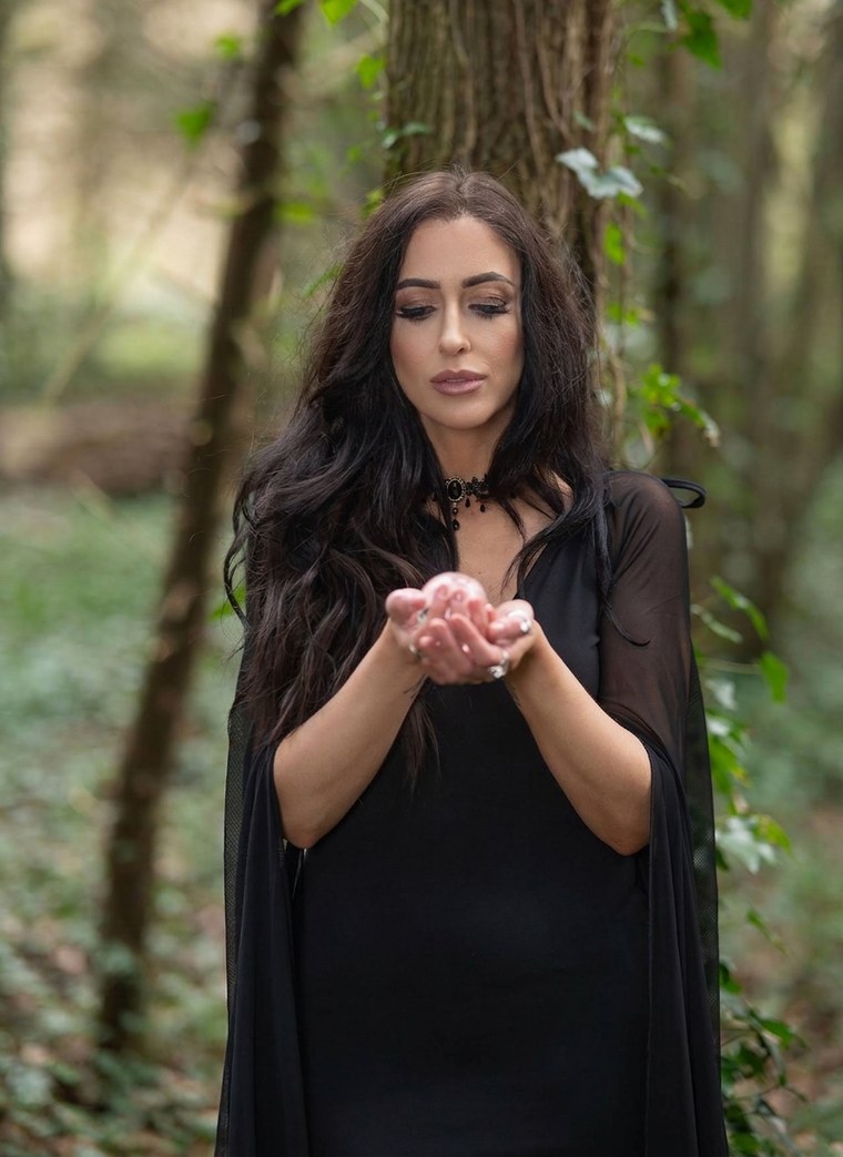 Emily, tarot reader, holding a crystal in cupped hands in a woodland